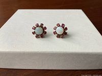 Front view of both earrings showing central opals and surrounding rubies