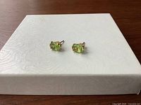 Top-down overview of both earrings on textured white surface showing peridot color and shape
