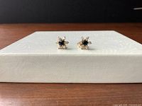 Front view of the pair of 14K gold earrings with blue sapphire center and imitation diamond accents, displayed on a textured white surface