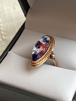 Ring displayed at slight angle inside black jewelry box on white cushion showing marquise cabochon top view.