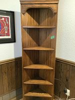 Full front view of vintage wooden corner bookcase unit showing five triangular shelves and arched detail at the top.