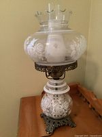 Full view of the vintage hurricane lamp showing etched rose floral glass globes, glass chimney, and ornate metal base on wooden table.