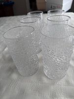 Set of six clear vintage Iittala drinking glasses showing textured water droplet pattern on all sides, arranged on fabric surface.
