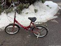 Full side view of red Schwinn Tango folding bicycle on pavement with snow background
