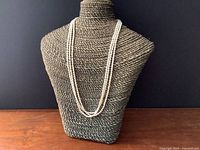 Triple strand vintage freshwater pearl necklace displayed on a bust against a dark background