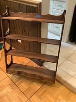Front view of vintage wooden plate rack on floor showing four shelves and bottom drawer