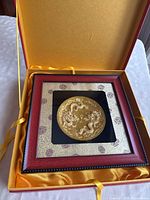 Framed gold leaf commemorative dish with two dragons, presented inside yellow satin lined box.