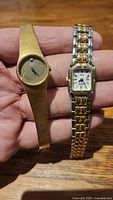 Two ladies wristwatches shown side by side, one with a gold-tone textured band and round face, the other with a bi-color gold and silver-tone band and rectangular face.