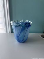 Side view of tall blue art glass vase showing clear glass with blue swirls inside and ruffled top edge