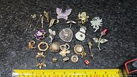 Top-down view of entire collection of brooches and pins arranged on granite surface, showing a variety of designs and sizes.