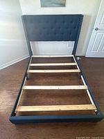 Full bed frame with dark blue fabric upholstery, button tufted headboard, and wooden slats visible inside the frame.