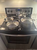 Full view of Henckels stainless steel cookware set displayed on stovetop including multiple pots and pans with lids.