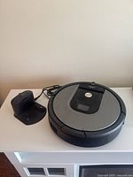 Photo showing Roomba robot vacuum and charging dock on white surface.