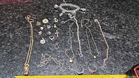 Overview of assorted pendants, rings and necklaces laid out on a dark countertop with measuring tape for scale, showing variety of shapes and sizes