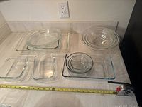 Eight clear Pyrex glass dishes arranged on counter with measuring tape for scale.