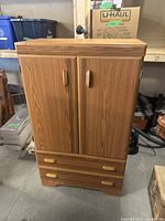 Photo of closed two-door wood-tone clothing cabinet with two drawers.