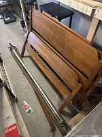 Two wooden double bed frames including headboards, footboards, and metal side rails placed on a concrete floor.