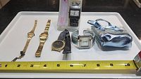 Lot of six untested wristwatches of various styles and sizes including metal and leather bands and a small blue tote bag.