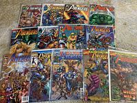 Photo showing all 13 Avengers Volume 2 comic books laid out on carpet, some angled. Covers feature classic Avengers characters including Thor, Hulk, Captain America, and Scarlet Witch.