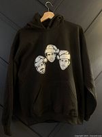 Full front view of black hoodie showing cartoon faces of Jonas Brothers wearing Santa hats.