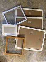 Six assorted picture frames arranged on carpet, showing backs and edges