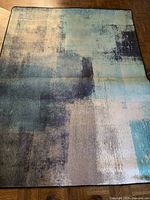 Photo showing the thin blue area rug with abstract pattern laid flat on parquet floor.
