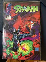 Front cover of Spawn Issue #1 comic book shows main character with red cape and green flame effects, with Image Comics logo and issue details.
