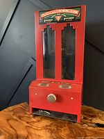 Front angle view of the vintage red coin-operated chewing gum dispenser showing two transparent columns and the coin slot with dispensing knob.