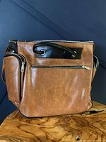 Front view of vintage tan brown leather camera bag with black zipper trims and handle, placed on wooden surface with dark background.