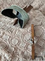 Side and front angle view of stereoscope with metal visor and wooden base on textured fabric.