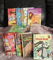 Photo showing nine children's storybooks arranged on a surface with a dark background. Books include Pinocchio, Finding Nemo, My Big Magic, The Lion King, The Piglet's Big Movie, How to Train Your Dragon, Dinosaurs, and two editions of The Jungle Book.