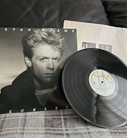 Vinyl record partially on album cover showing Bryan Adams close-up portrait in monochrome.