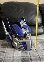 Side view of blue and silver Optimus Prime talking mask with measuring tape showing approximately 12 inches height.