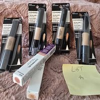 Seven CoverGirl makeup products including four TruBlend It's Lit liquid concealers and three boxed items on a soft pink fabric background, some packaging is loose.