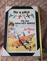 Front view of the framed Hot Birds print showing colorful toy plane illustrations and promotional text.