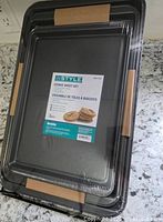 Photo of sealed 3-piece cookie sheet pan set packaging with visible label showing brand, features and sizes.