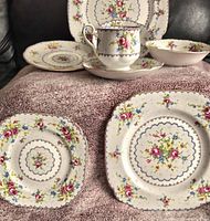 Close-up image showing various pieces of Royal Albert Petit Point china including plates, cup, saucer, and bowl, placed on a textured cloth.