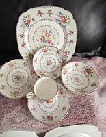 Photo showing the full china set including large plate, smaller plates, bowl, saucers, and teacup, all featuring floral Petit Point pattern and gold trim