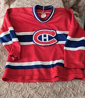 Front view of vintage child's Montreal Canadiens hockey jersey in red with blue and white stripes and logo.