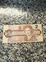 Front side of 1986 Canadian 2 dollar bill showing Queen Elizabeth II portrait, denomination, and serial number.