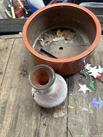 Top down view showing frosted glass vase next to ceramic plant pot with drainage hole inside. Both items show wear and dirt.