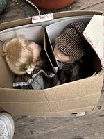 Two porcelain dolls inside a cardboard box, showing their faces and clothing partially visible.