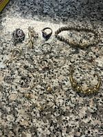 Full collection of jewelry pieces: rings, bracelet, earrings, necklace, and pins on granite surface