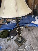 Side view of the traditional table lamp showing beige fabric lampshade and an ornate bronze/gold-toned base with decorative details.