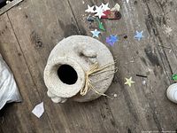 Top-down view of beige ceramic vase showing textured surface, neck opening, and raffia tie on rustic wooden background.
