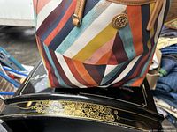 Close up of handbag exterior showing multicolor diagonal stripe pattern and Tory Burch logo medallion on front.