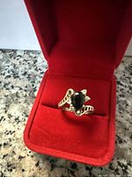 Full view of the vintage silver ring with central black stone, sitting in a red velvet ring box against a granite surface.