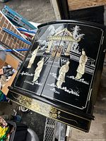 Front angled view of the medium-sized lacquered wood vintage box showing black glossy finish, painted Asian women figures, and gold ornamental detail.