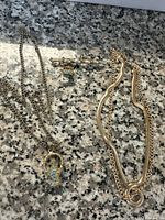 Photo of vintage jewelry set including gold-tone bar pin with pearls and crown charm, pendant necklace with turquoise stones, and two gold chains on granite surface.