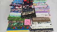 Stacked cotton quilting fabric pieces in a variety of colors and prints including stars, florals, leopard patterns, and mixed designs with a label '25' visible
